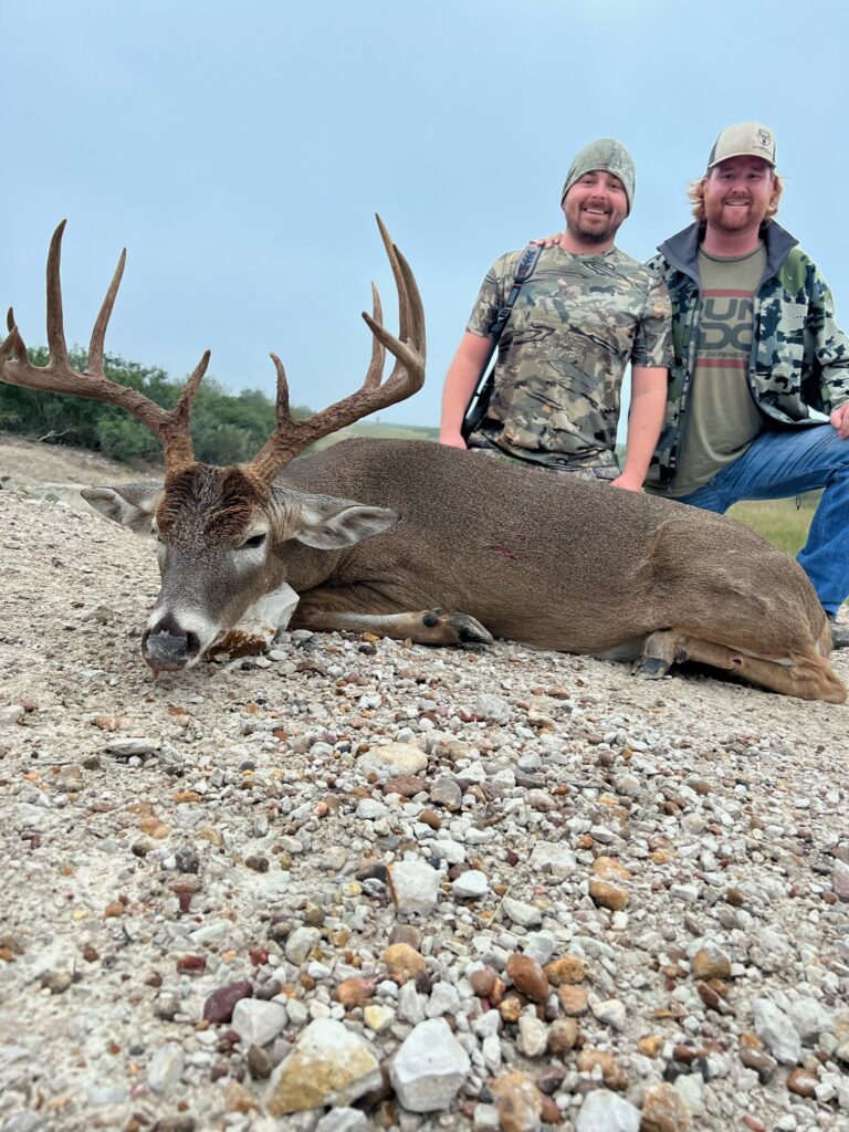 Two hunters posing with a large deer they have hunted.