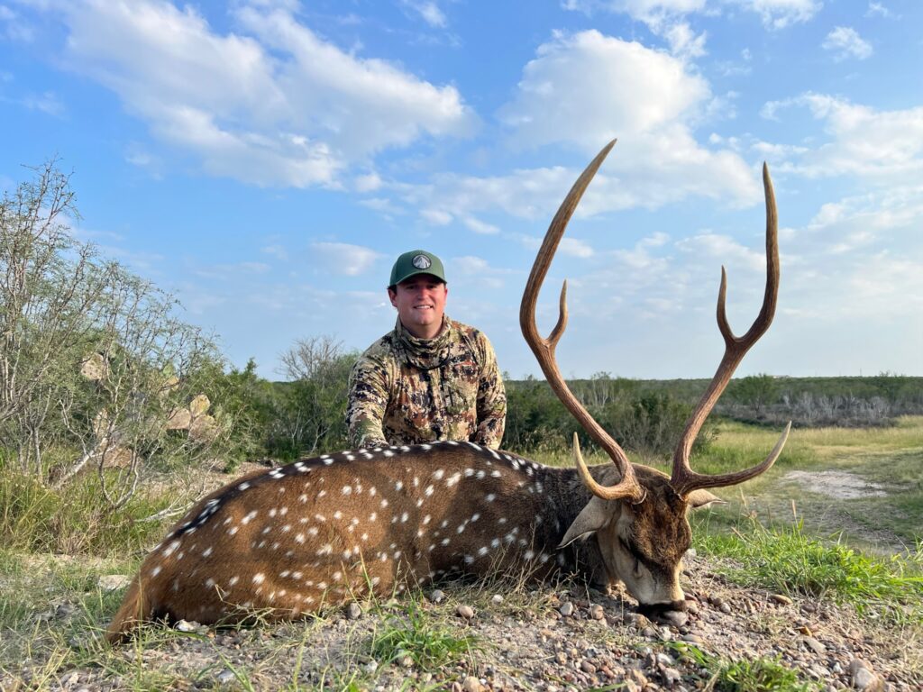 Hunter posing with a large deer under a blue sky.