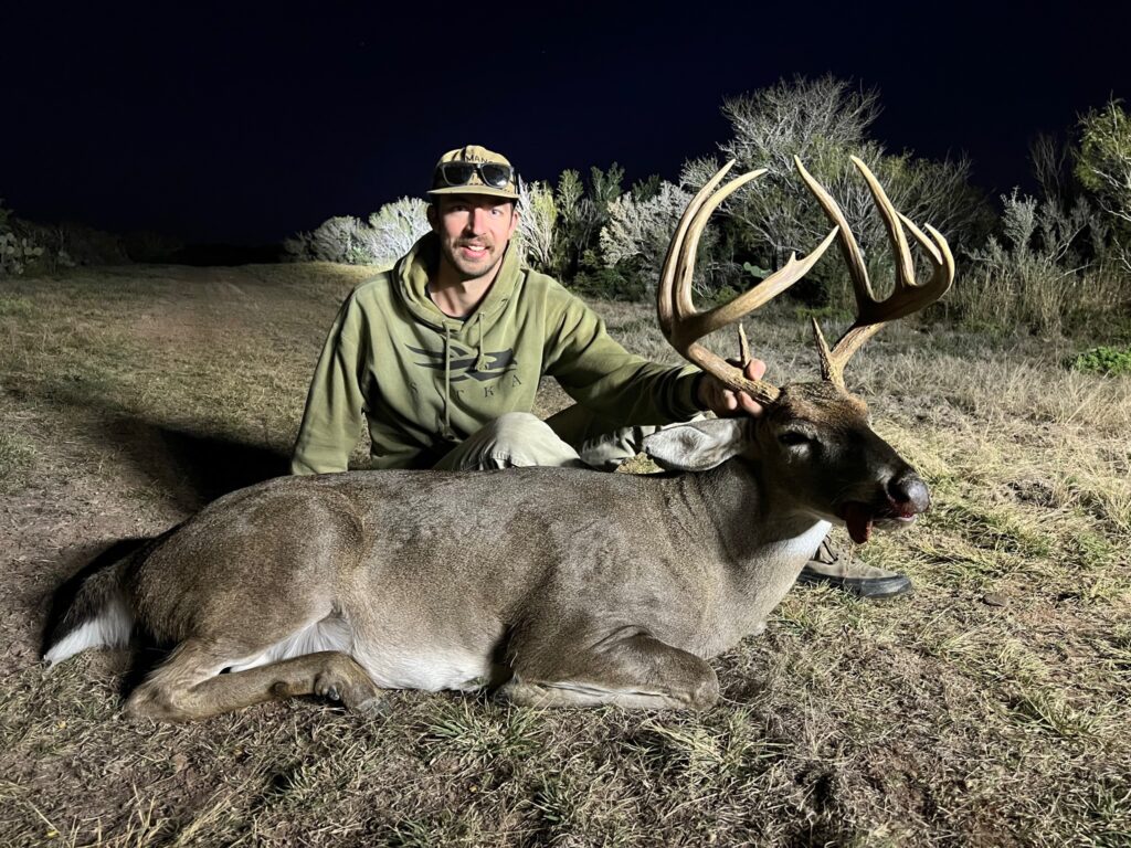 Hunter posing with large buck deer at night.